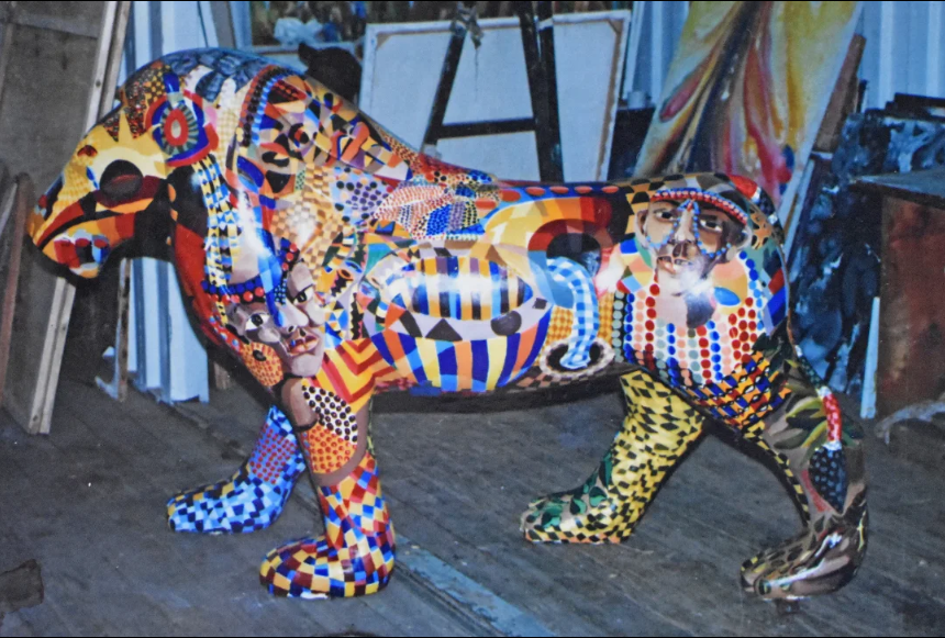 Colorful painted leopard sculpture with geometric and figurative motifs in a studio.